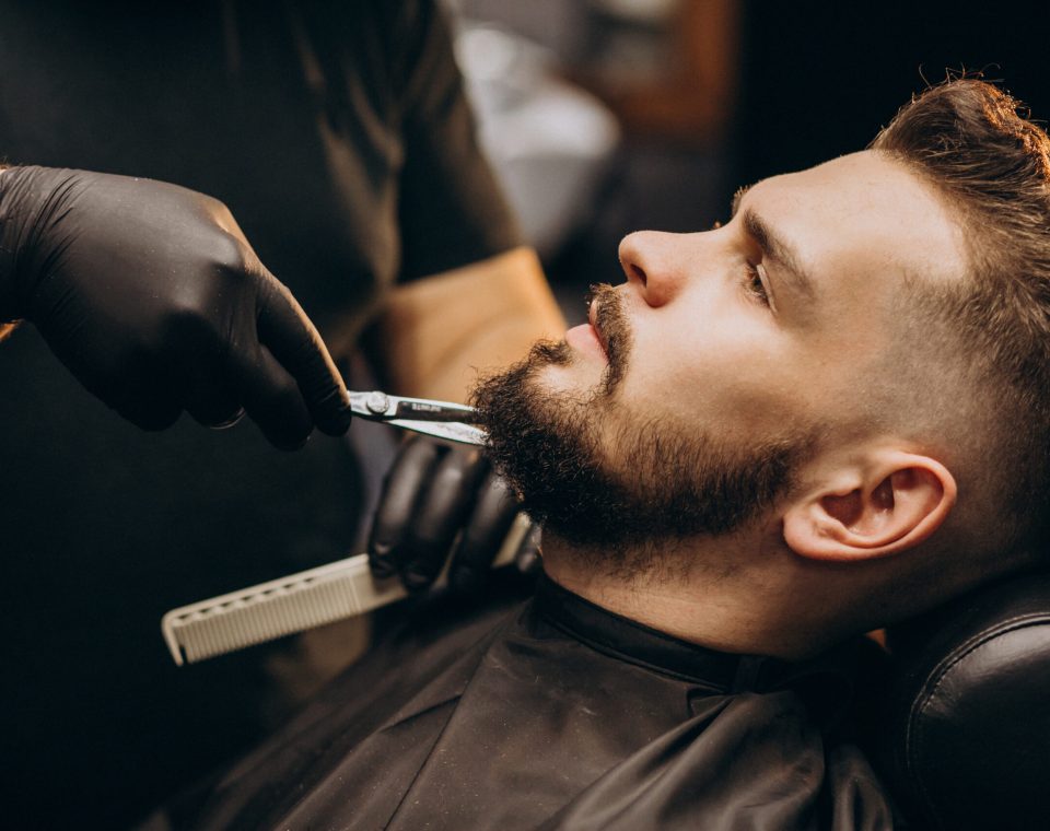 Handsome man cutting beard at a barber shop salon